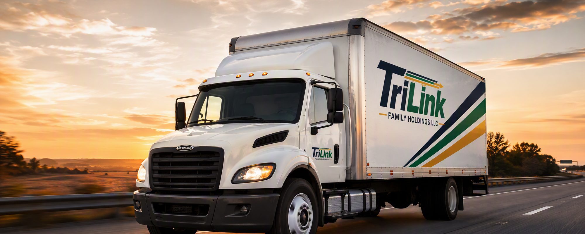 A TriLink 26-foot box truck photographed from the side on the interstate, showing the cab, sleeper area and box body.